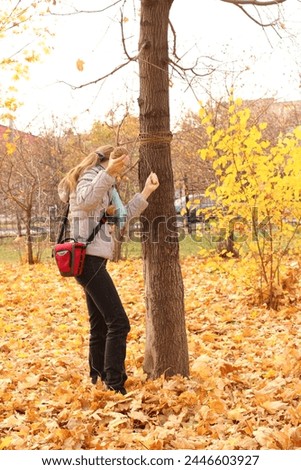 Girl in autumn park wraps trees