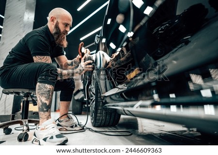 Professional vehicle polishing and detailing service in a modern car workshop. Brightly lit workspace with large led lights. High quality car valeting concept. Royalty-Free Stock Photo #2446609363