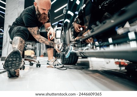 Professional vehicle polishing and detailing service in a modern car workshop. Brightly lit workspace with large led lights. High quality car valeting concept. Royalty-Free Stock Photo #2446609365