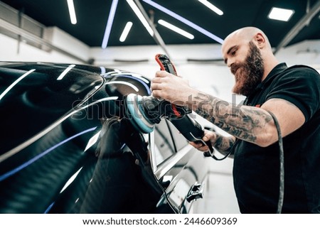 Professional vehicle polishing and detailing service in a modern car workshop. Brightly lit workspace with large led lights. High quality car valeting concept. Royalty-Free Stock Photo #2446609369