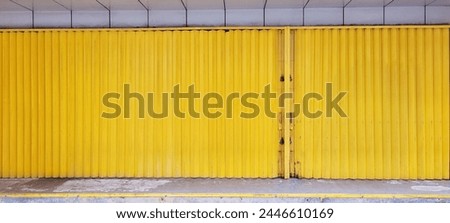 Closed yellow metal rolling door of a shop, adding a vibrant pop of color to urban streetscape. Illustrating the modernity and vibrancy of commercial spaces.