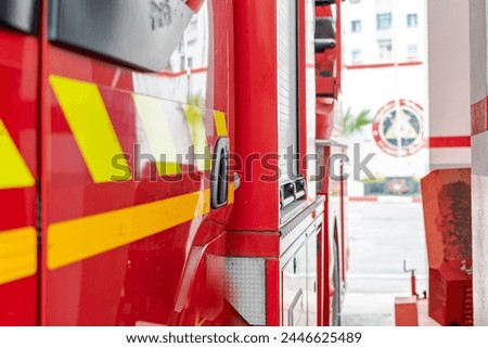 Lateral side of a fire truck in a fire station, red colored door and yellow fluorescent strips. Selective focus and narrow depth of field, blurred Algerian firefighters logo in background.