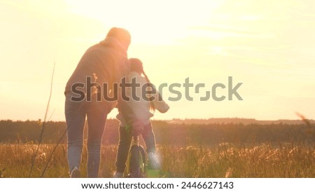 Woman teaching girl to ride bike, silhouettes at sunrise. Exciting activities with family, older, mom and daughter spend time together. Playful interesting form of learning to ride bike. Fun childhood