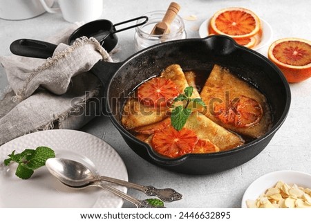 Crepes with Orange Sauce in a cast iron pan. Traditional French crepe Suzette with orange sauce on light table Royalty-Free Stock Photo #2446632895