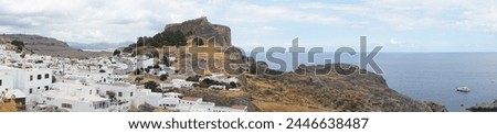 Photo panorama. View of the white buildings of Captains houses of the 16th-18th centuries and the ancient Acropolis of Lindos in August. Lindos is an archaeological site, a fishing village. Greece