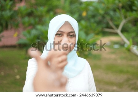 Portrait of Asian female model wearing blue hijab making love symbol with fingers