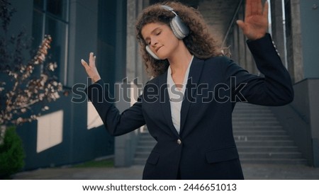 Joyful carefree girl Caucasian business woman listening music in headphones earphones on street outdoors happy businesswoman lady dancing moving listen song walking from office in city friday freedom