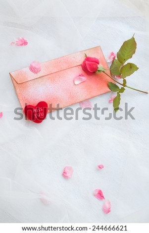 Valentine's Day background: pink rose, pink rose petals,plush heart "Miss you",red envelope on a transparent fabric. Free space for a text