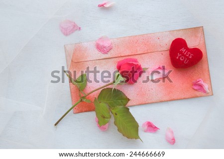 Valentine's Day background: pink rose, pink rose petals,plush heart "Miss you",a red envelope on a transparent fabric.