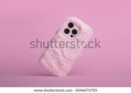 iPhone 15 Pro max in pink fluffy fur case falls down back view, phone case mockup with three cameras in monochrome colours isolated on pink background