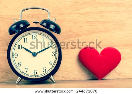 Concept alarm clock with red valentine heart on wood board background. Retro filter.