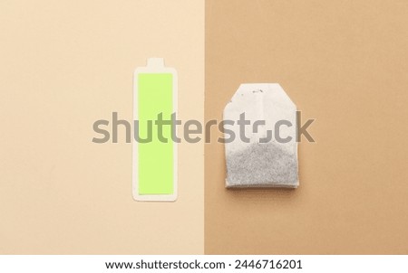 Tea bag and fully charged battery on beige background Royalty-Free Stock Photo #2446716201