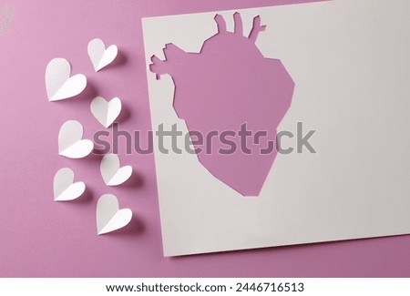 Paper-cut hole in the shape of an anatomical heart and a lot of hearts on pink background. Creative idea, love concept