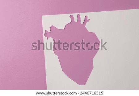 Cut paper hole in the shape of anatomical heart on pink background. Heart health concept