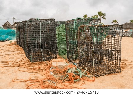 Lobster pots and tangled ropes on a sandy beach with palm trees in the background.