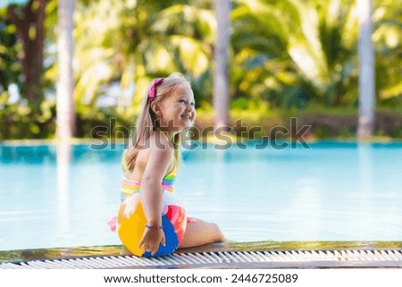Child in swimming pool with inflatable toy ball. Kids swim. Colorful rainbow float for young kids. Little girl having fun on family summer vacation in tropical resort. Beach and water fun. 