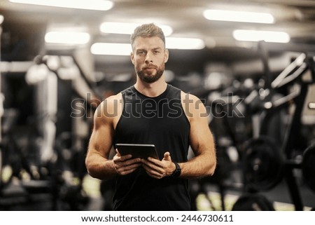 Portrait of a personal trainer standing in a gym with tablet in his hands and looking at the camera. Royalty-Free Stock Photo #2446730611