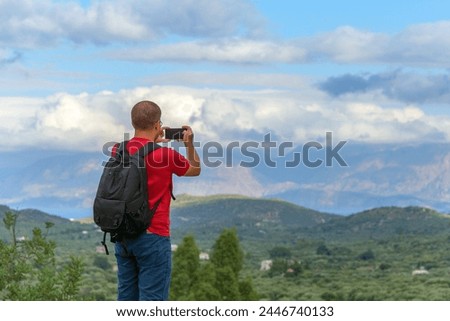 A male traveler takes pictures of the beautiful landscape of the island of Crete on a smartphone.