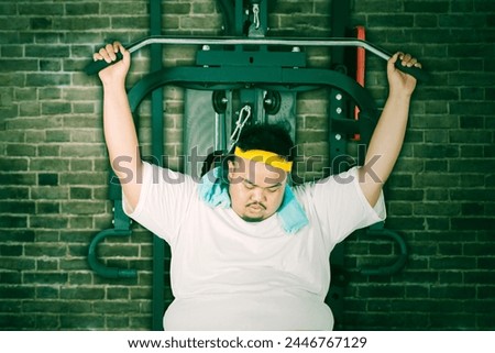 Picture of young obese man looks lazy exercising in a gym