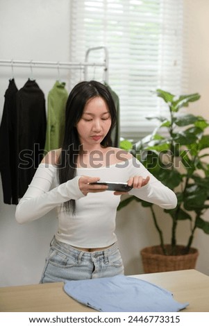 Young business woman takes a photo of a cloth with her smartphone device to put it up for sale on a second-hand clothing platform. online selling concept