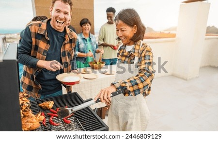 Happy multiracial friends having fun cooking healthy food with barbecue at rooftop house outdoor - Multigenerational people grilling chili and chicken during summer weekend meal  Royalty-Free Stock Photo #2446809129