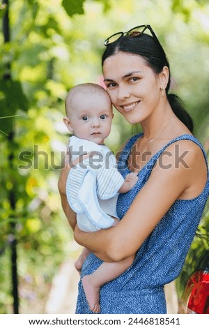 A beautiful young smiling woman holds a small child, her son, in her arms outdoors in nature. Photo of a happy family, portrait of people.