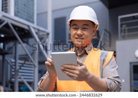 A smiling Asian man is working on a construction site. foreman, foreman. Standing outside and using a tablet. Close-up photo.