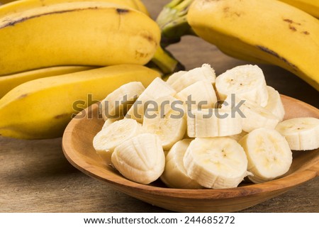 A banch of bananas and a sliced banana in a pot over a table. Royalty-Free Stock Photo #244685272