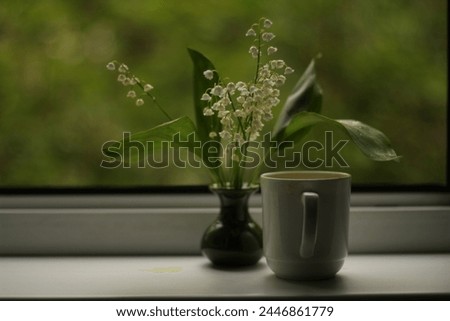 Bouquet of lilies of the valley in a green vase in summer with coffee on the windowsill