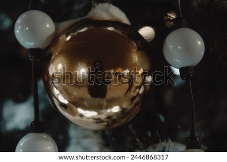 The image is a close-up of a gold ball, possibly used as a Christmas tree ornament. It is indoors and is illuminated by light.