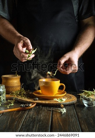 Tea made from dried linden and chamomile flowers for colds in the hands of a man on the kitchen table. Traditional medicine concept made from beneficial and medicinal herbs. Royalty-Free Stock Photo #2446869091
