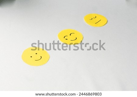 Smiling face, flat face and crying smiley face emojis drawn on yellow round paper, copy space, isolated white background.