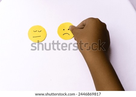 boy's hand placing flat face and sad face emoji he drew on yellow round paper, isolated white background