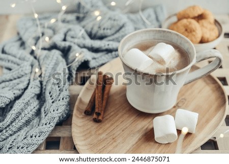 Mug with cocoa and marshmallow, knitted scarf, cinnamon, cookies, decorated with led lights. Hygge concept Soft focus - Image