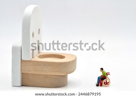 miniature figurine of a disabled man on a wheelchair looking at a huge wc