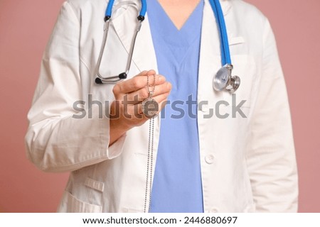 Woman doctor holding a Buddhist religious symbol, studio pink background. Nurse in uniform with stethoscope on red studio background