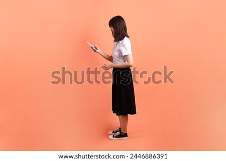 Cheerful female student in Thai university uniform with gesture of Holding mobile phone isolated on orange background. International Students' Day, World Students' Day. Gen Z