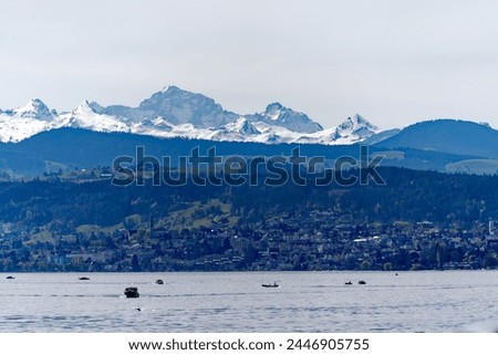 Lakeshore of Lake Zürich with trees and snow covered Swiss Alps in the background at Swiss City of Zürich on a blue cloudy spring day. Photo taken April 5th, 2024, Zurich, Switzerland.
