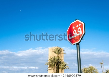 Detail of a "Stop" traffic sign written in Arabic with the complex of the Royal Mausoleum of Mohammed V and the minaret tower of the ancient mosque of Sultan Yaqub al-Mansur in the background Royalty-Free Stock Photo #2446907579