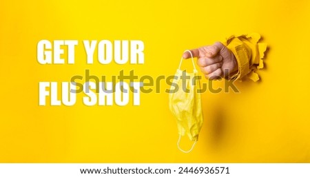 A person holding a yellow mask with the words get your flu shot written below. The image has a playful and lighthearted mood, encouraging people to get vaccinated against the flu