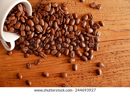 coffee grilled beans on old retro vintage aged yellow brown wooden table with a white cup on texture board table background Empty space for inscription 