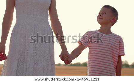 Child mom walking in summer park in sun, family happiness concept. Child, son, mom holding hands, mothers kid. Happy family relaxing in nature. Loving Parent, child boy, walking together on sunny day