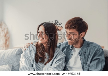 One dream for two of us. Romantic millennial spouses relax on couch together looking aside imagining happy future life. Young man and woman in love cuddling indoors creating plans on weekend vacation