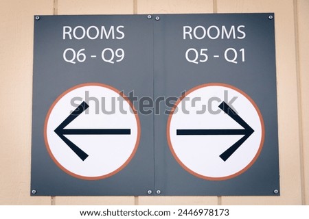 A sign on a wooden wall with arrows directing to different rooms with room names and number. A wall sign with directions
