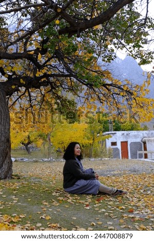 An Asian female tourist posing for a picture with the beautiful scenery of the colorful foliage at a local village in Passu Valley, Gilgit-Baltistan, Pakistan.