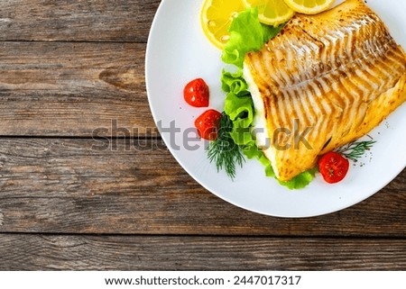 Fried cod loin and fresh vegetables on wooden table 