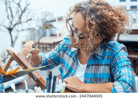 Young beautiful adult woman painter creates pictures, drawing with paints on canvas in modern workshop. Professional occupation, creative hobby, activity for soul, vocation, develop skills concept