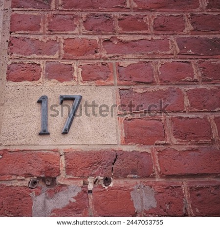Number with the number seventeen or 17 in Latin. An old red brick wall with signs of destruction. Covered with cracks. Non-uniform surface texture. Royalty-Free Stock Photo #2447053755