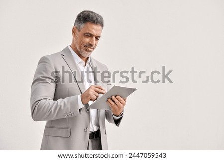 Happy mature business man using digital tablet isolated on white background. Busy middle aged businessman ceo wearing suit, older businessman professional executive looking at pad working on tab tech. Royalty-Free Stock Photo #2447059543