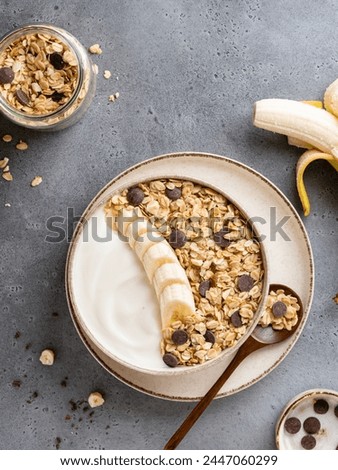 Chocolate nuts granola bowl with natural greek yogurt served with banana slices. Healthy morning breakfast. Sugafree vegetarian meal. Top view food. Gray background. Copy space.